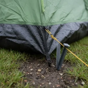 Close-up of a heavy-duty waterproof groundsheet and a metal tent peg secured into the damp British soil.
