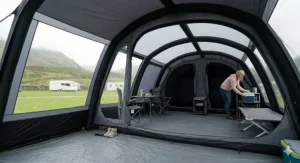 Wide-angle interior view of a spacious Kampa tent living area with camping furniture, internal air beams, and a view of the fells through the window.