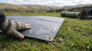 A camper using a garden hose to wash mud and grass off a durable tent footprint after a weekend camping trip in the UK.