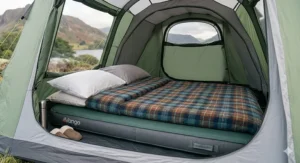 A double camping mattress for a tent styled with a traditional British tartan wool duvet and pillows inside a modern green family tent.