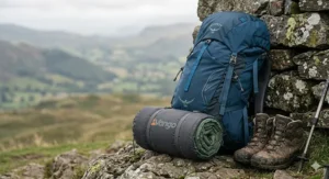 A lightweight, rolled-up camping mattress for tent trekking, strapped to a rucksack leaning against a dry stone wall in the British countryside.