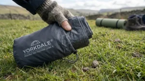 A lightweight and compact tent footprint being folded and placed into a small grey carry bag for easy backpacking.