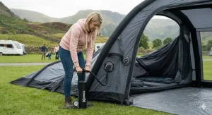 A camper using a manual hand pump with a pressure gauge to pitch a Kampa inflatable air tent on a grass pitch in the UK.