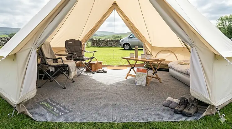 A photorealistic interior view of a premium canvas bell tent on a grassy UK campsite, showing a grey breathable tent carpet laid out with camping chairs, a wooden table, and an Ordnance Survey map under soft daylight. breathable tent carpet