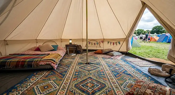 A colourful lightweight tent carpet for festivals spread across a bell tent floor, styled with cushions and fairy lights for a UK summer music festival. lightweight tent carpet for festivals