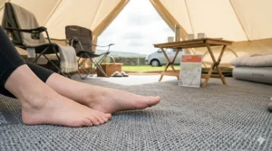 A close-up view of bare feet resting on the soft, padded texture of a breathable camping carpet inside a tent, highlighting comfort and insulation.