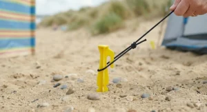 Versatile sand pegs holding down a sun shelter and picnic blanket on a breezy day by the British seaside.