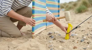 Step-by-step guidance on inserting beach tent pegs at a 45-degree angle to secure a classic windbreak.