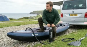 A paddler preparing for a lakeside trip, using a high-pressure double action pump camping to inflate a tandem inflatable kayak on the shore.