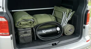 A compact double action pump camping neatly packed alongside sleeping bags and camp chairs inside the boot of a family car.