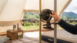 A person's hand adjusting the position of an oscillating clip-on fan on a tent pole.