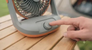 A hand adjusting the speed setting dial on a portable battery powered tent fan.