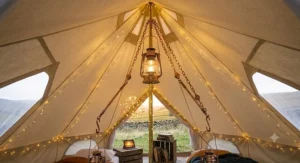 An interior view of the canvas tent looking from a different angle, showing string after string of warm LED fairy lights intricately woven along the internal poles and a rustic rug, creating a beautiful and cosy ambiance.