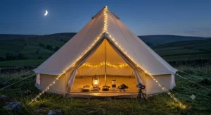 A stunning external night photograph of a single glowing canvas bell tent pitched on a field in the UK hills. Warm, soft light spills from the open door and windows, illustrating the final, peaceful and welcoming lighting setup.
