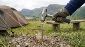 Close-up demonstrating proper mallet usage to securely drive a heavy-duty steel peg into gravelly ground.