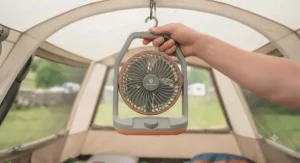 A person holding a compact battery powered tent fan up inside a camping tent.