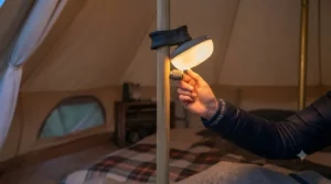 A hand adjusting the dimmer switch on a tent light to create a soft, cosy glow for evening comfort.