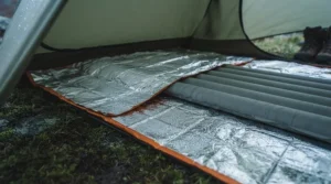 The thermal blanket is laid out flat inside a tent, serving as an insulating and waterproof ground sheet beneath a sleeping mat.