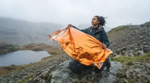 A hiker in distress waves the high-visibility orange side of a thermal blanket as a signal on a remote hillside.