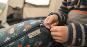 Child's hand easily pulling the smooth, snag-free zip on a colourful kids sleeping bag.