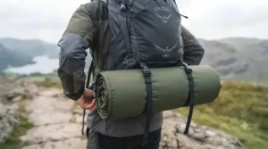 A hiker strapping a lightweight self-inflating sleeping mat to the base of a rucksack during a Highland hike in Scotland.