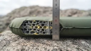 Side profile of a 5cm thick self-inflating sleeping mat cushioning a camper lying on hard ground.