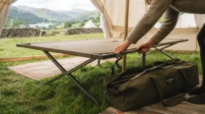 A packed raised camp bed in its carry bag next to camping gear, ready for a weekend trip.