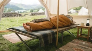 A warm sleeping bag laid out on a comfortable raised camp bed inside a glamping bell tent.