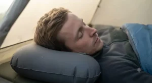 Side profile view of a person sleeping soundly on an ergonomically contoured inflatable camping pillow designed to cradle the neck while under canvas.