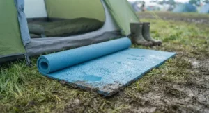 Waterproof roll mat repelling morning dew and damp grass outside a tent at a soggy UK festival site.